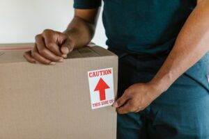 pexels-photo-7464731-7464731 A person handling a moving box with a 'caution this side up' label indoors.